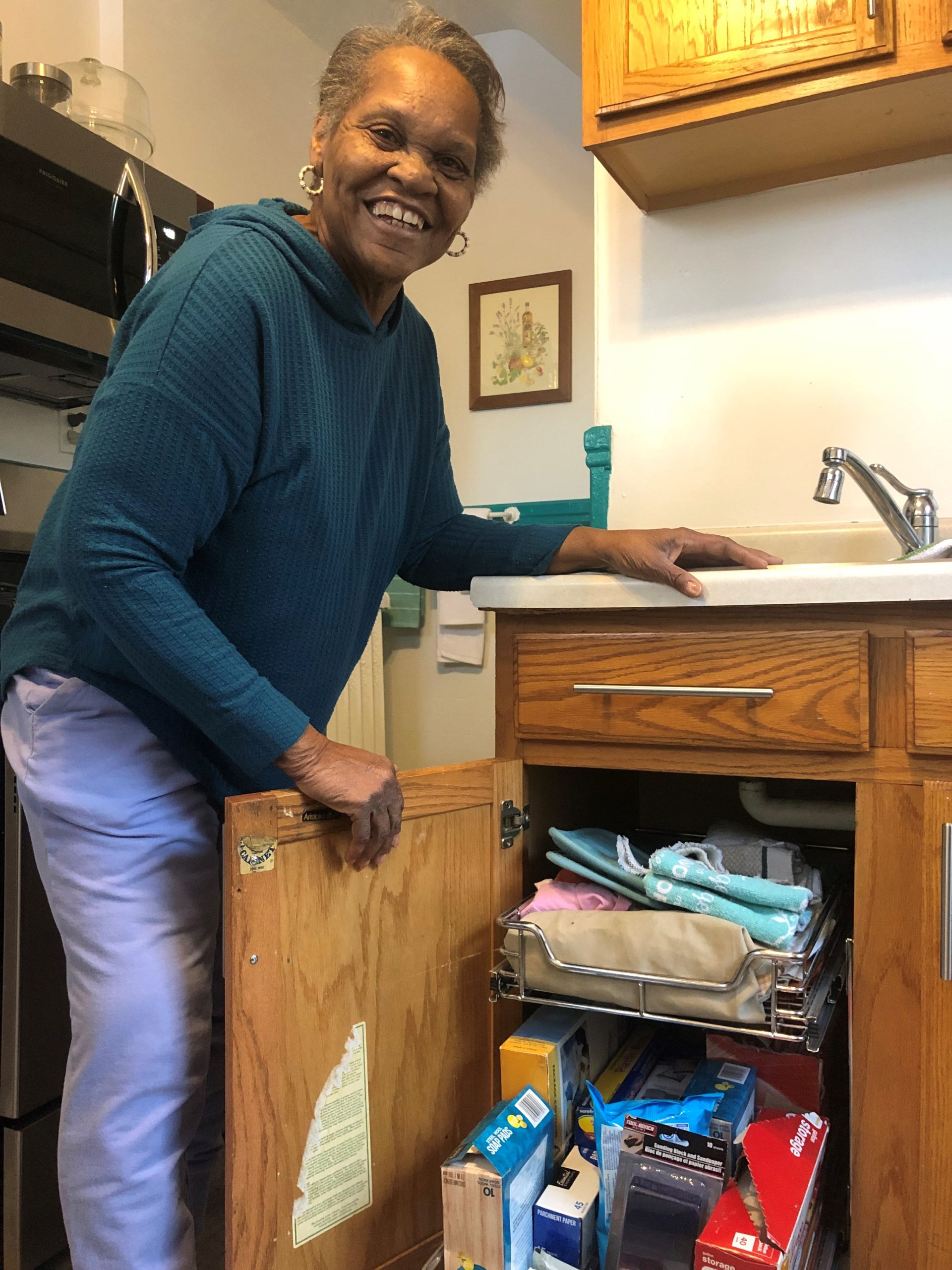 a woman stands next to a cabinet. The door is open and the shelves are overflowing with things