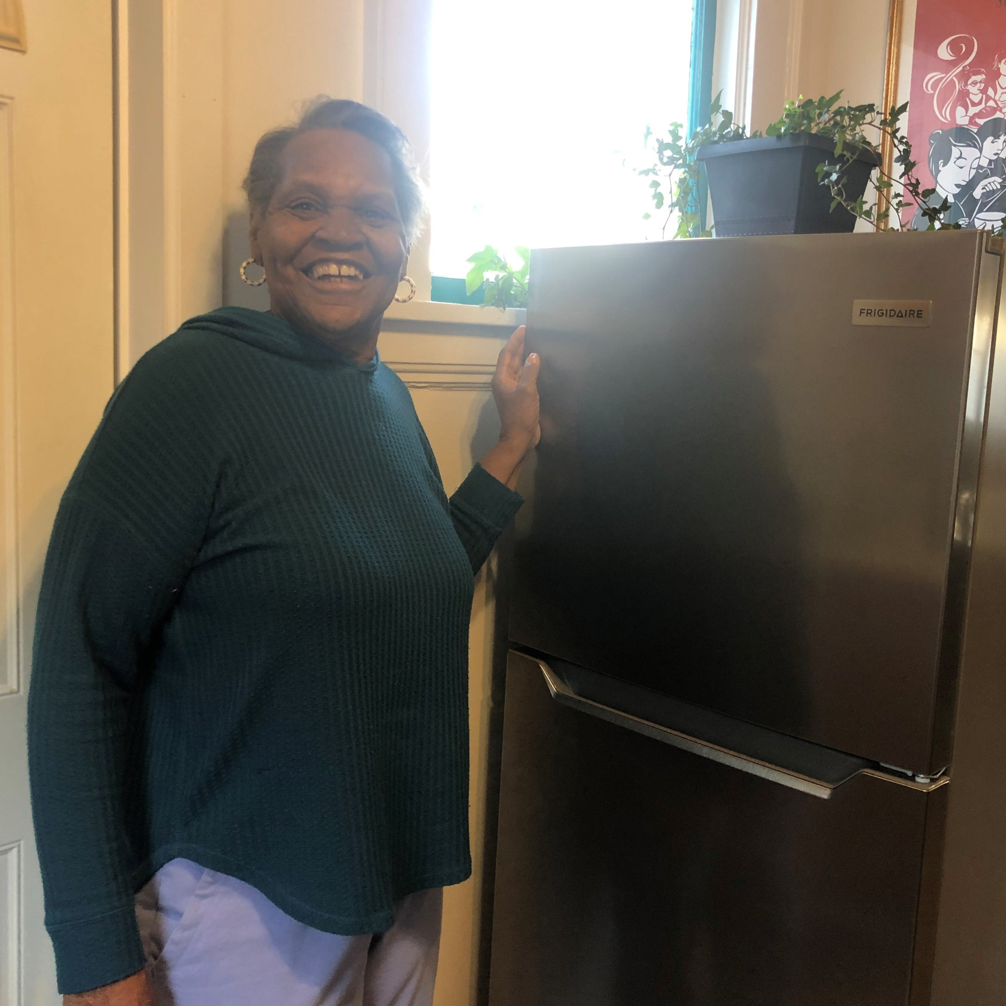 a smiling woman stands beside her new refrigerator